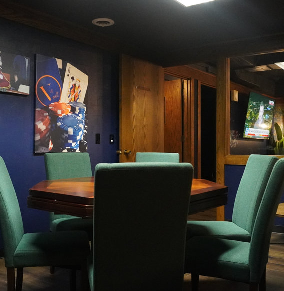 Wooden table with green chairs, colorful art on blue walls, and wooden doors in coworking dining area.