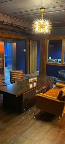 Orange chairs at dark table under starburst chandelier with blue walls and glass partitions in coworking space.