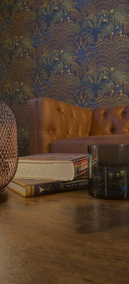 Orange tufted sofa with stacked books on wooden table against blue floral wallpaper in coworking lounge area.