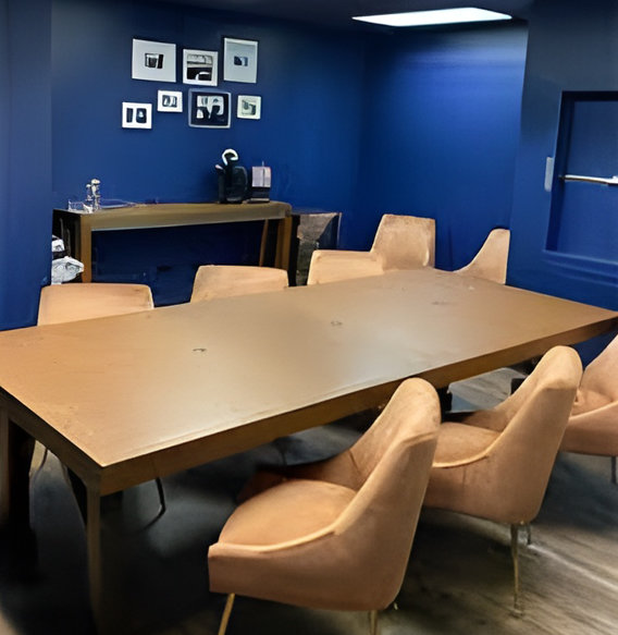 Conference room with wooden table, beige chairs, blue walls, framed art, and side table in coworking space.