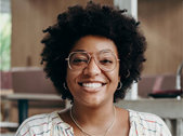 Woman with glasses and afro smiling in coworking space.