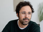 Man with beard and glasses in green shirt smiling in coworking space.