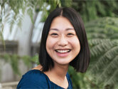 Woman with black hair smiling in blue top outdoors near coworking space.