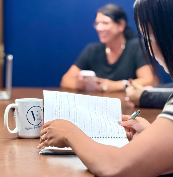 Three people meeting at table with branded mug, documents, and pens against blue wall in coworking space.
