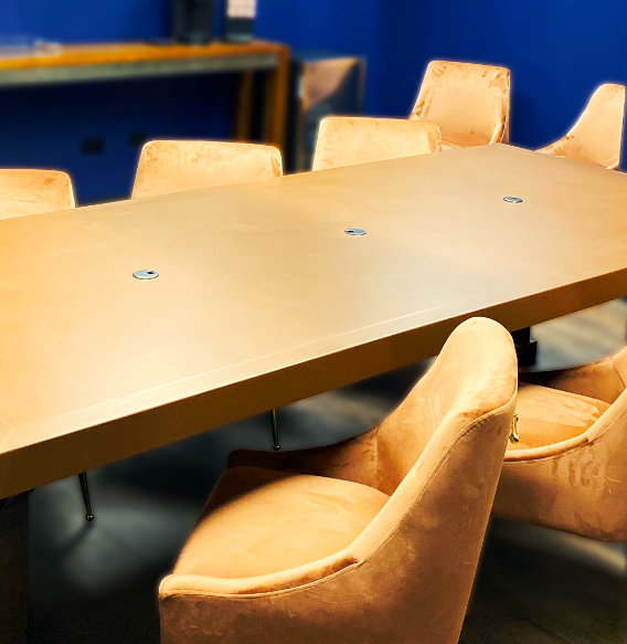 Wooden conference table with beige chairs and power outlets against blue walls in coworking meeting room.