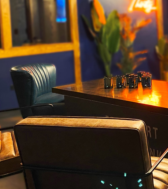 Lounge area with beige chairs, wooden table with glasses, blue walls, and warm ambient lighting.
