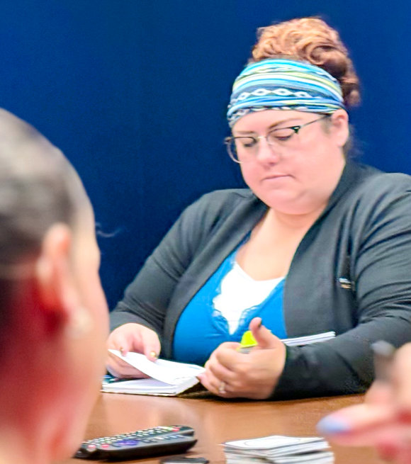 Woman with blue headband and glasses writing with highlighter at table with papers and calculator during meeting.