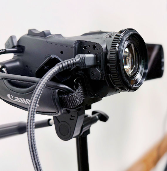 Canon video camera with microphone mounted on tripod against a white background.