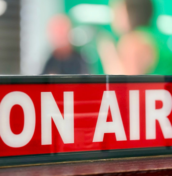 Red illuminated ON AIR sign with blurred green background in broadcast studio.